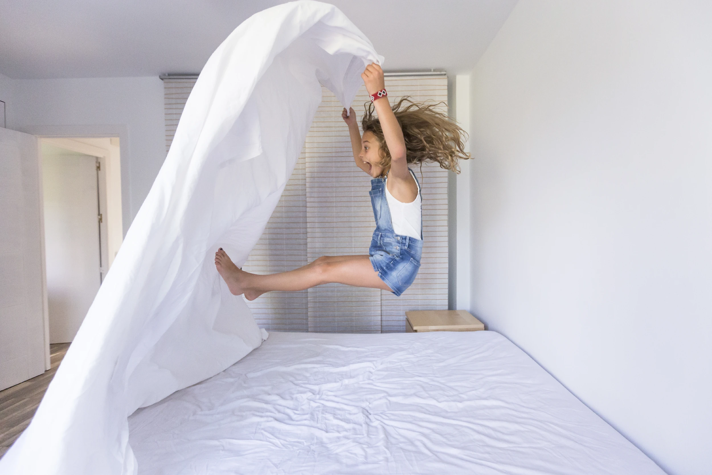 Petite fille jouant sur un lit avec du linge de lit blanc